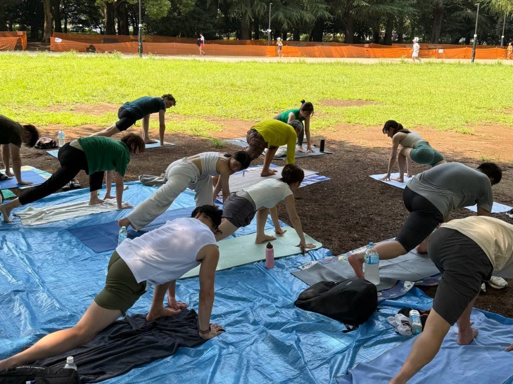 昼の公園でのグループレッスン。並んだマットの上で、全員が同じポーズをとっているところ